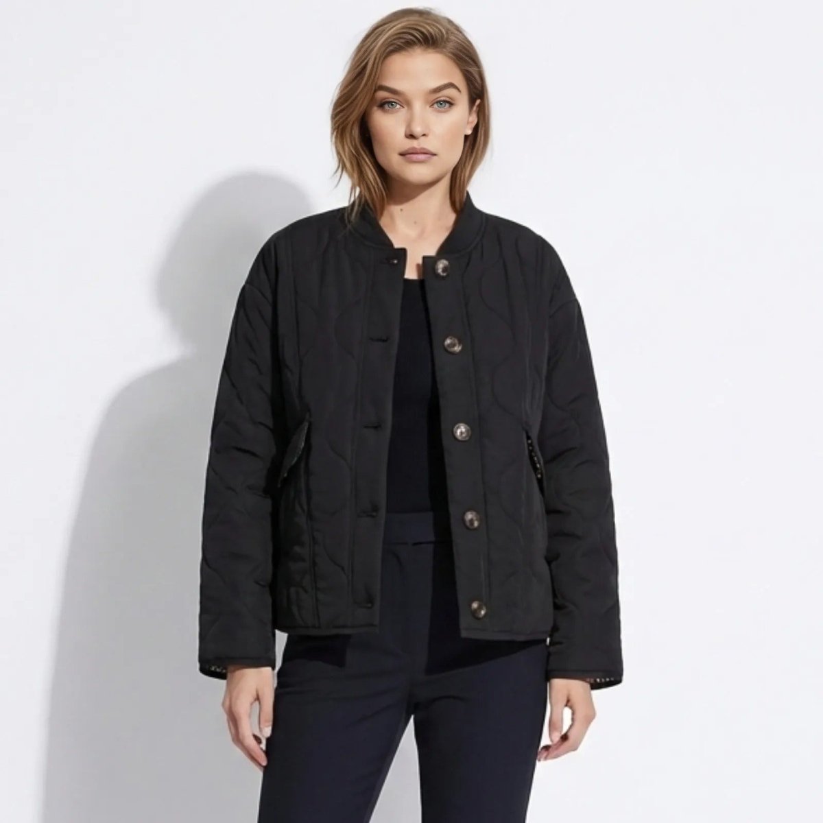 Model wearing the Kouvr Fashion black collarless quilted liner jacket with button front, styled with black trousers.
