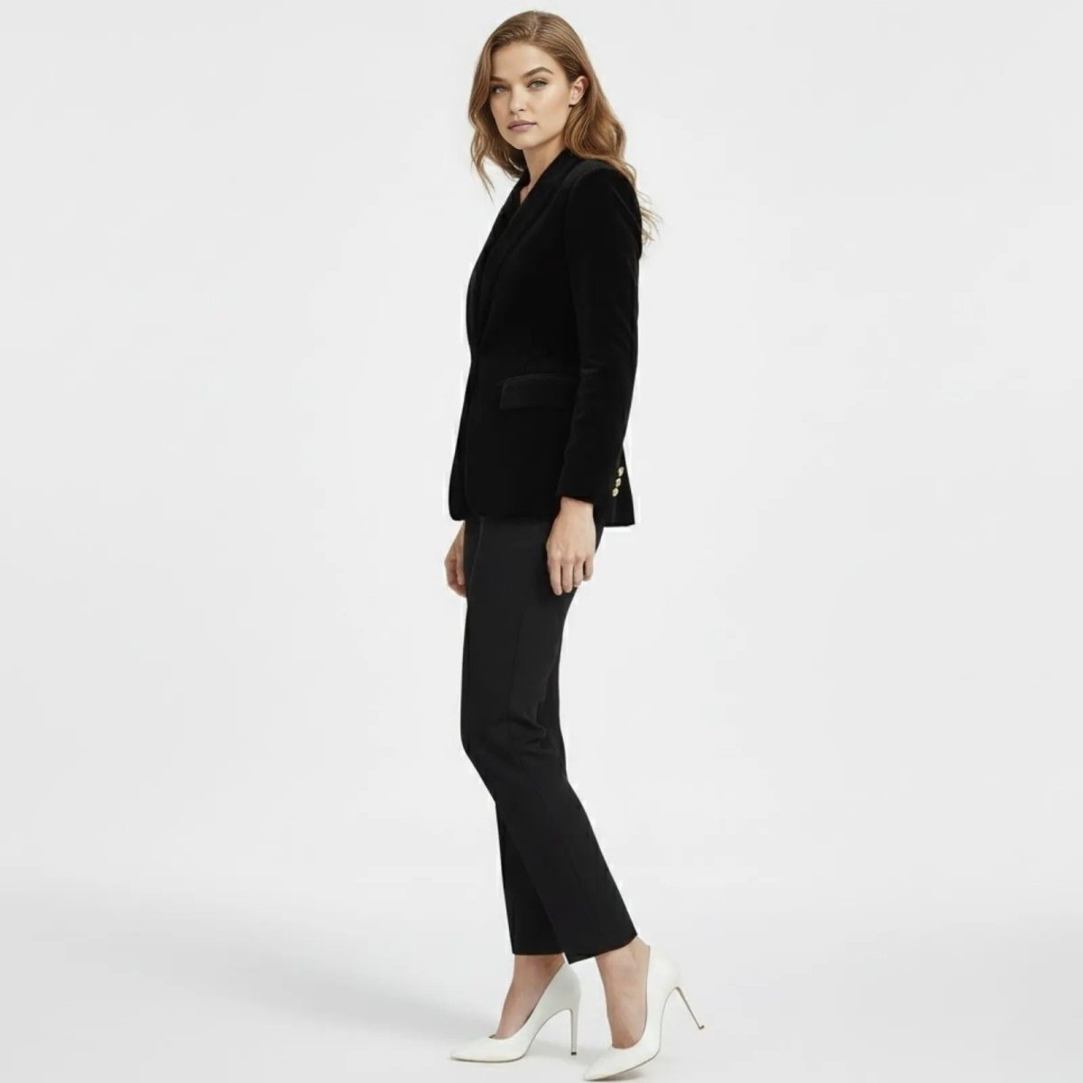 Side profile of a woman in a black luxury velvet blazer by Kouvr Fashion, showing the tailored fit and gold button cuff detail.
