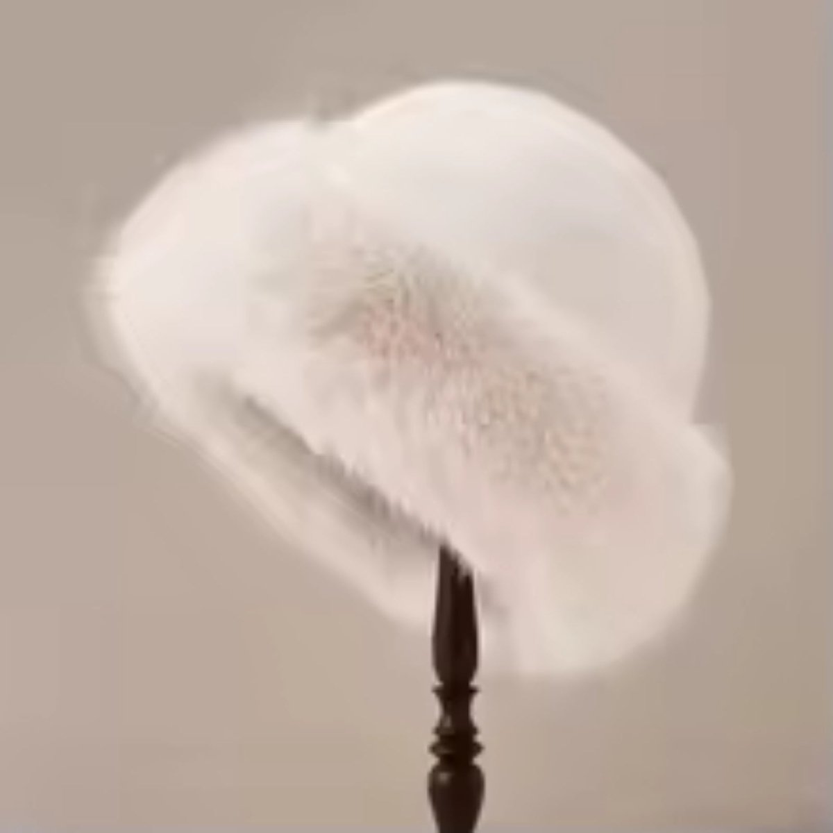 Beige feathered hat on a wooden stand against a neutral background