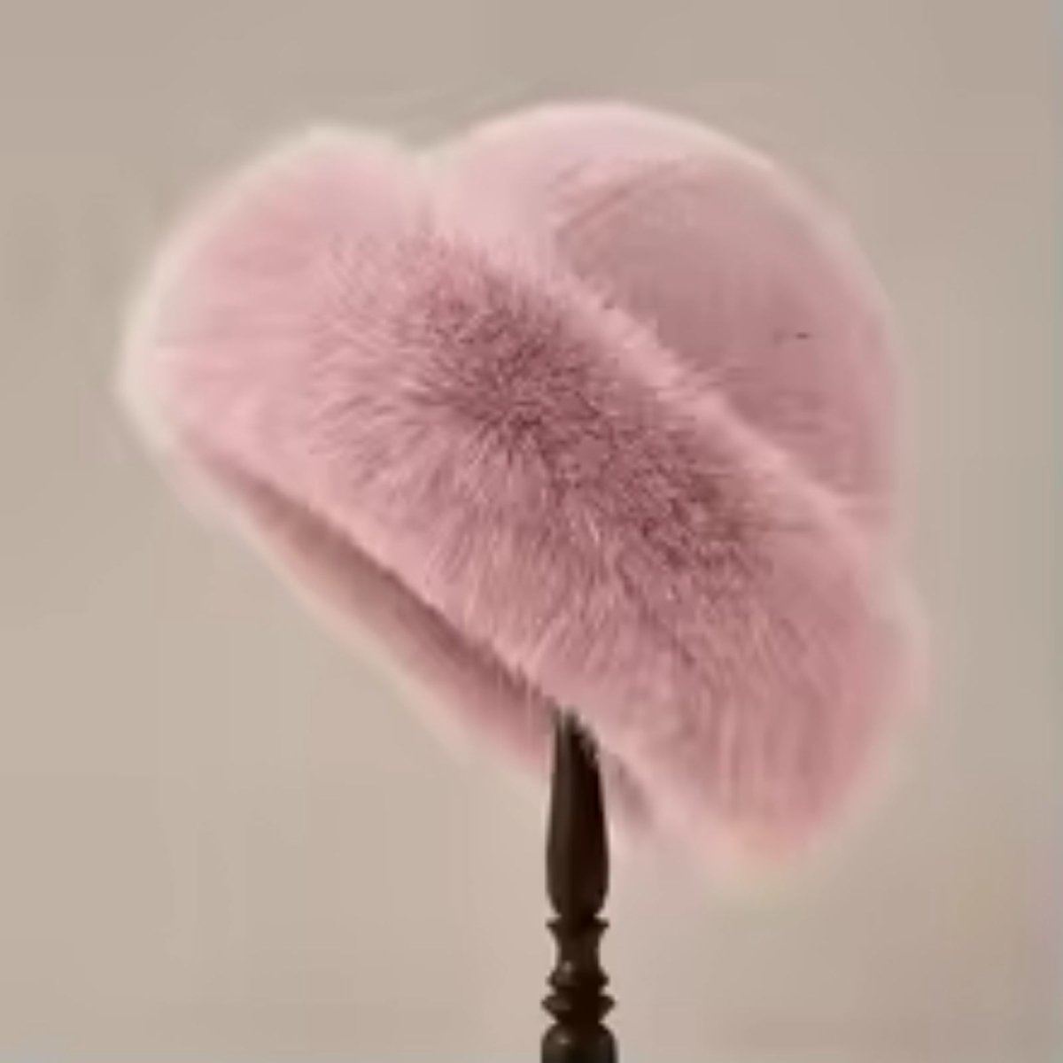 Pink fluffy hat on a stand against a neutral background
