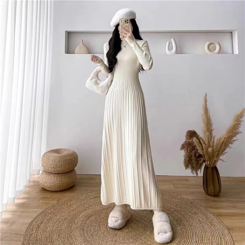 A woman wearing the Kouvr Fashion Dannah long sleeve pleated knit midi dress in ivory, styled with a white beret and fuzzy slippers in a minimalist room.