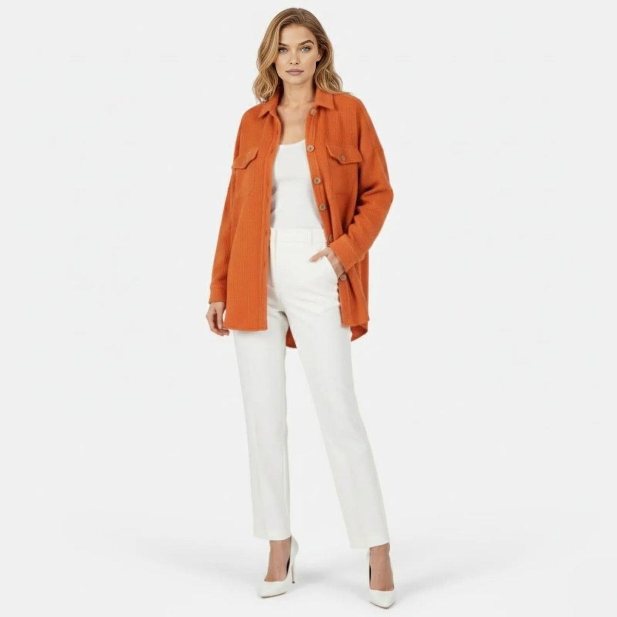 Woman wearing Kouvr Fashion's burnt orange oversized waffle knit shacket open over a white tank top and white trousers, standing forward.