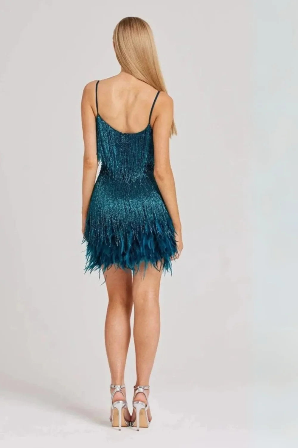 Model from behind wearing the Kouvr Elena teal mini dress, showing the movement of the metallic fringe and feather trim