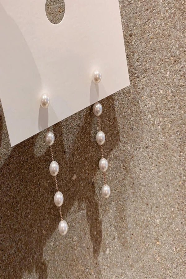 Pearl Kouvr earrings on a white card against a textured beige background