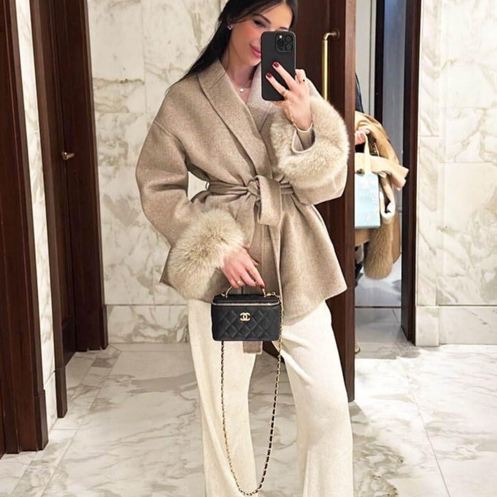 Woman taking a mirror selfie wearing the Kouvr Fashion beige wool coat with fur cuffs, styled with wide-leg pants and a designer bag.