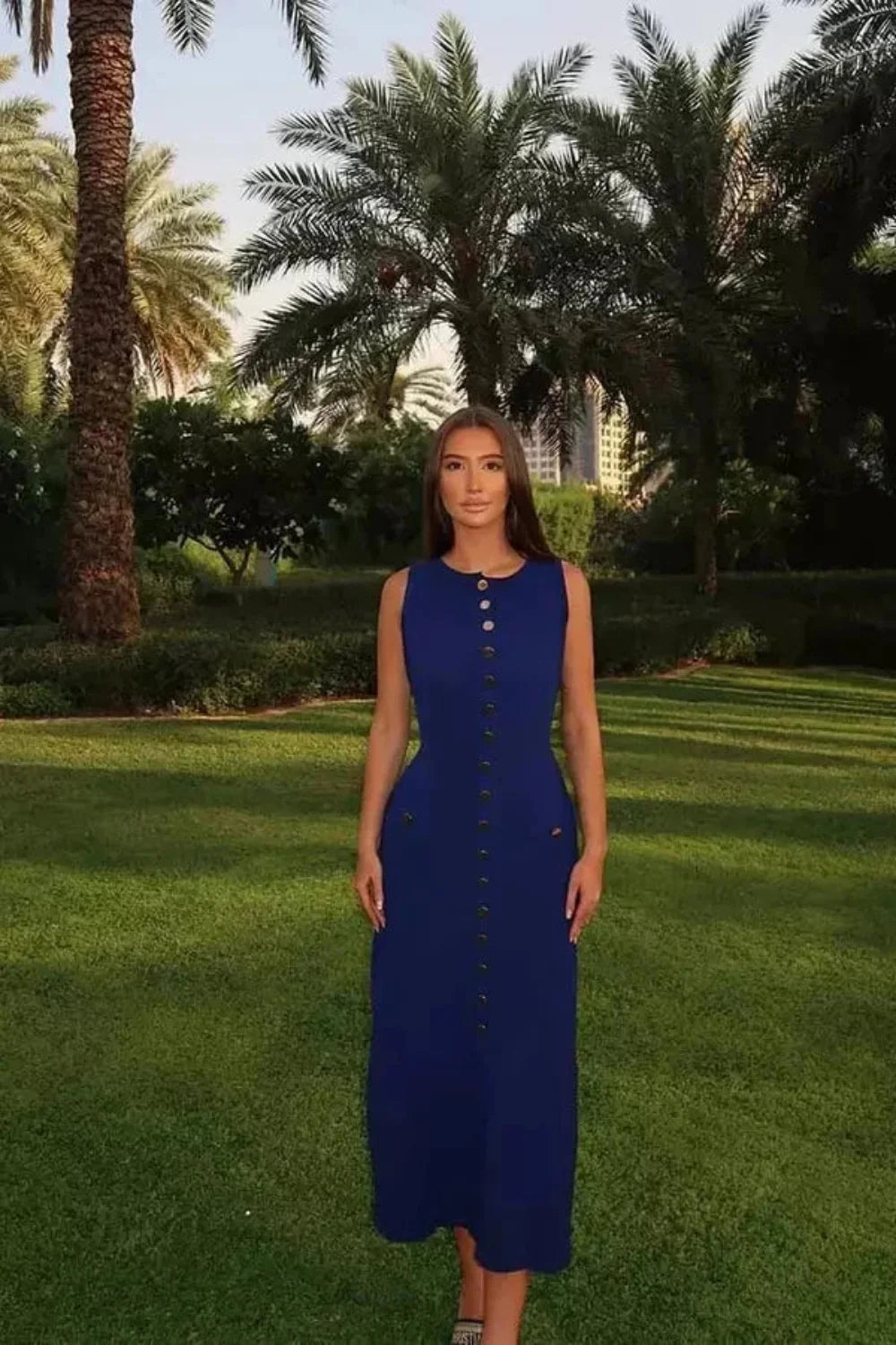 A woman wearing the Kouvr Fashion Fiorella blue sleeveless button-front midi dress in an elegant garden setting