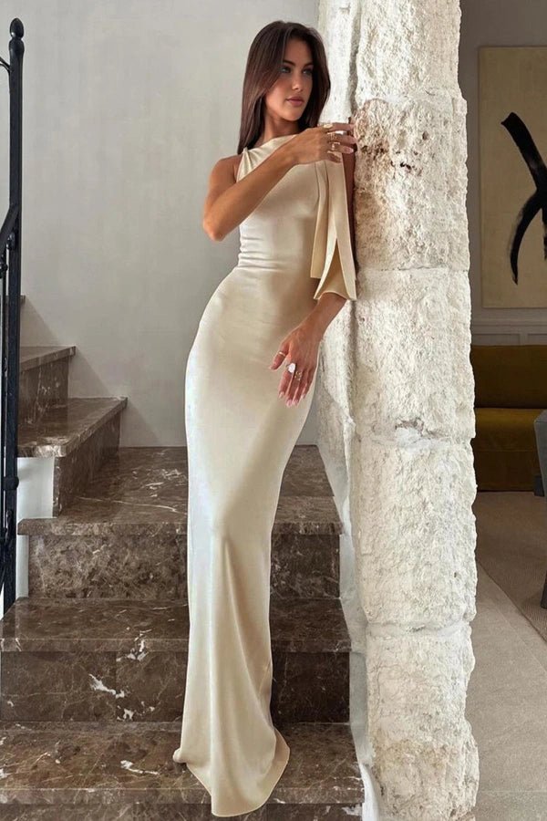 Model wearing the Jennie, a cream one-shoulder satin maxi gown, standing on a marble staircase.