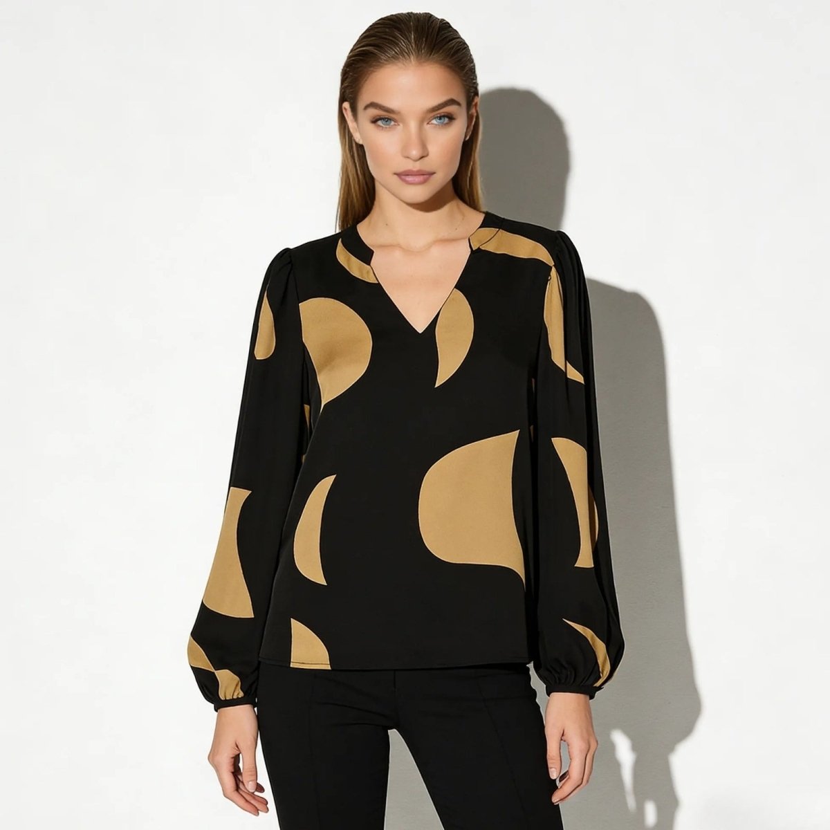 Model wearing the Judith black and tan abstract print blouse with long bishop sleeves and a V-neck, paired with black trousers.