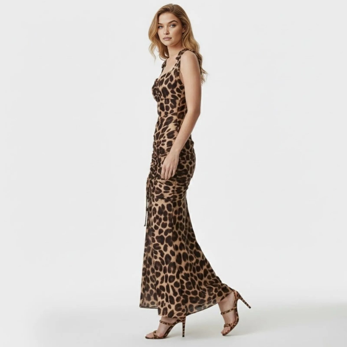 Side profile of a model walking in a floor-length, fitted leopard print dress with ruched detailing along the body.