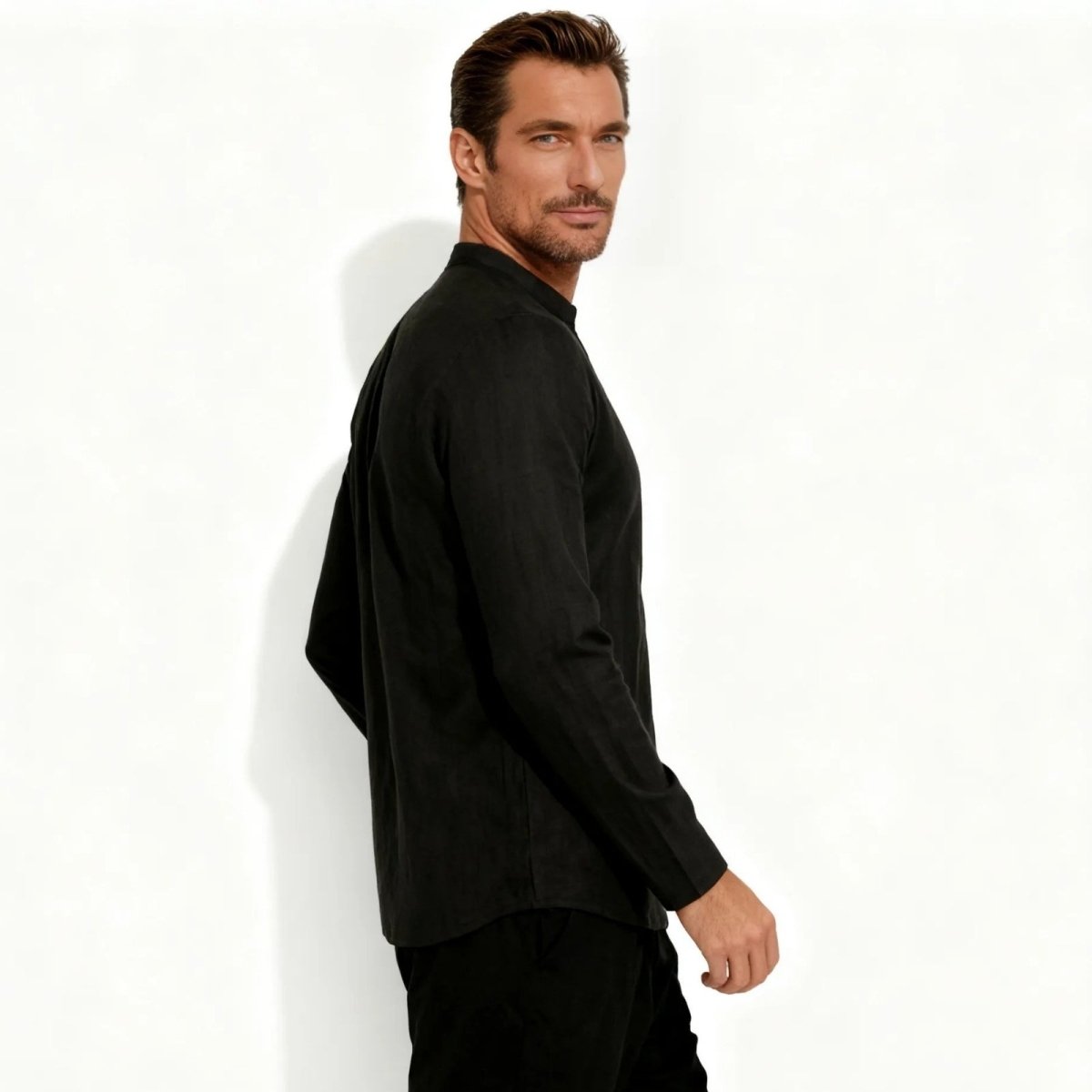 Male model in a black band collar linen shirt from Kouvr Fashion, looking over his shoulder to show the side profile and fit.
