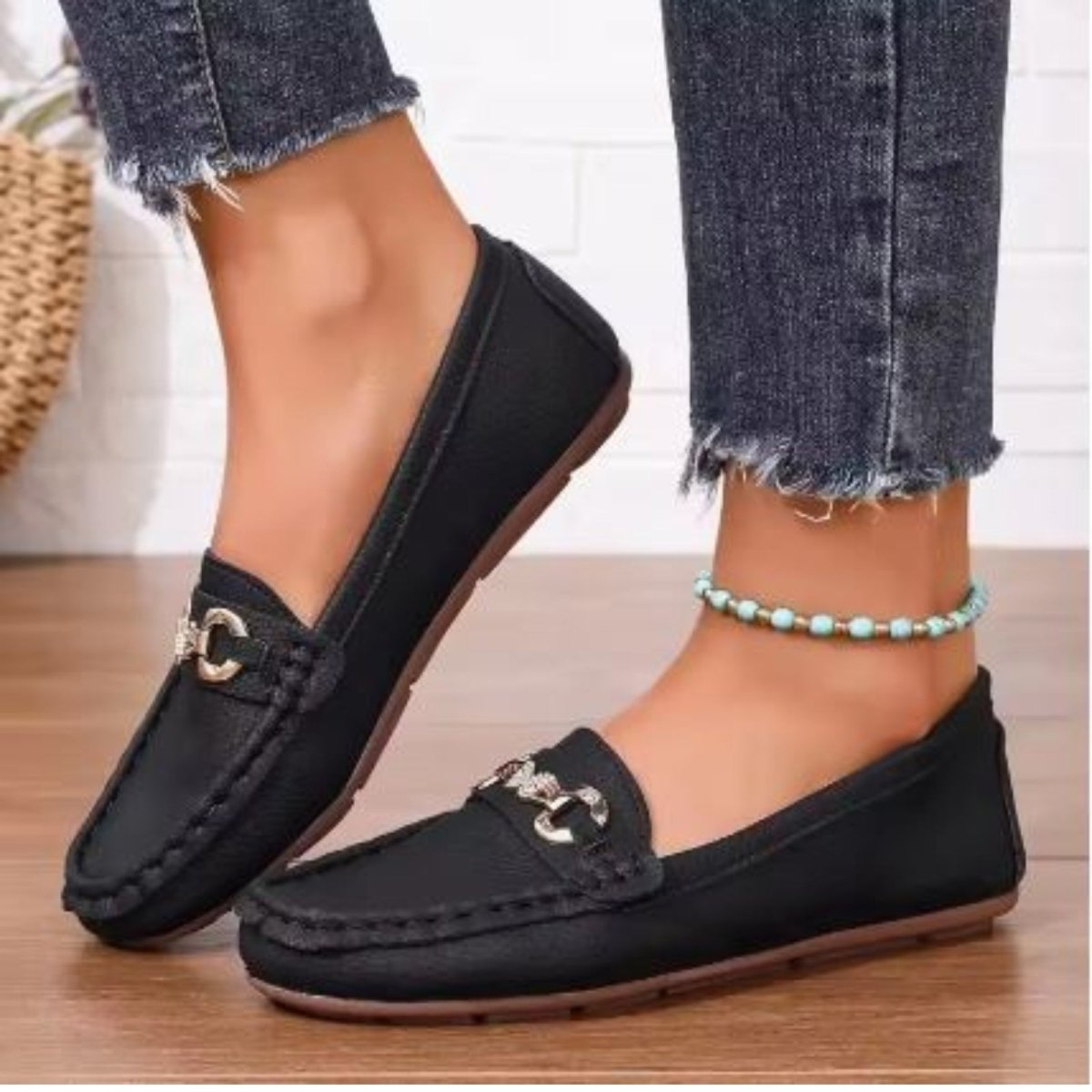 A woman wearing Kouvr Mildred black leather horsebit loafers with cuffed blue jeans and a gold anklet.
