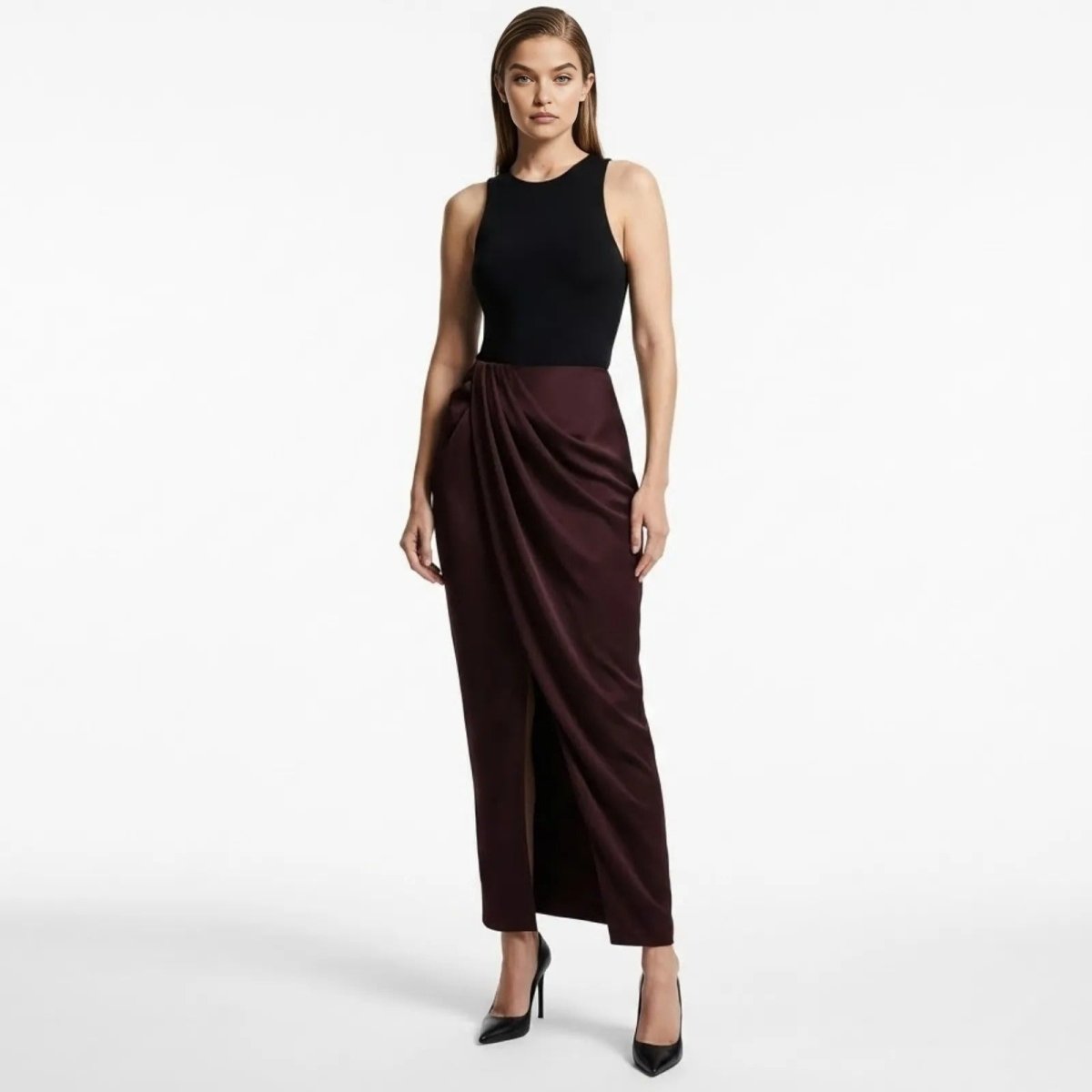 Model wearing Kouvr Fashion's Ourania high-waist draped sarong pants in deep aubergine satin, styled with a black tank top and heels.
