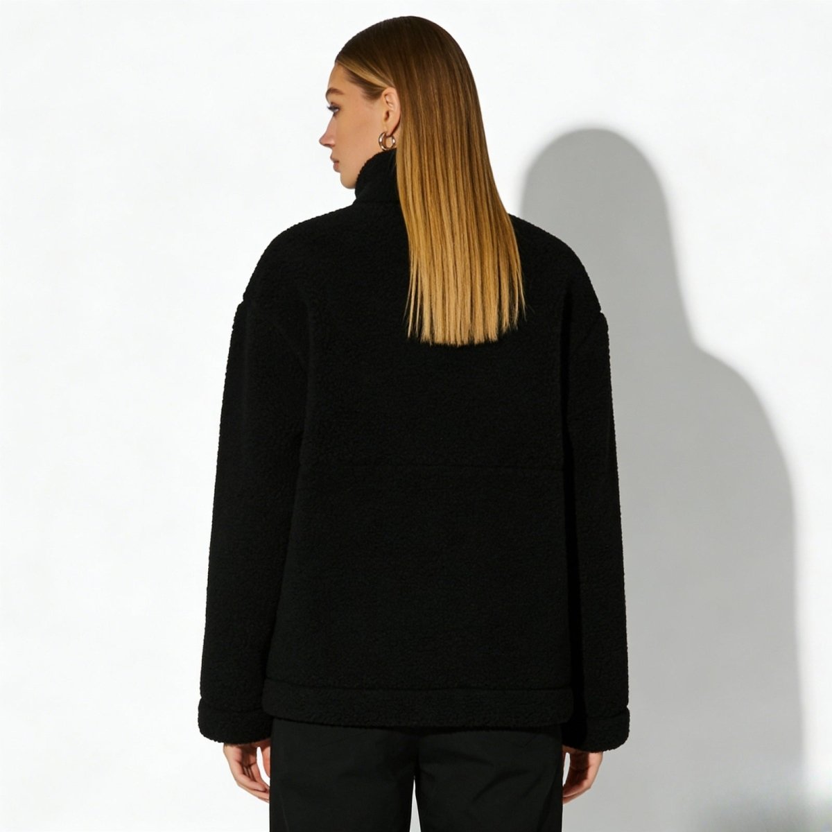Back view of a model wearing the Kouvr high-neck black fleece jacket, showing the clean seam details and minimalist silhouette.