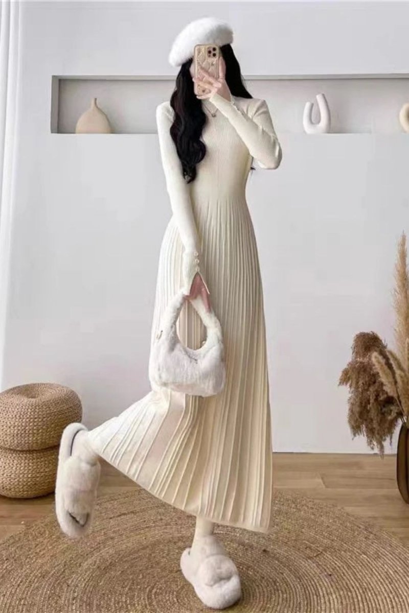 Model wearing the Kouvr Fashion long sleeve pleated knit maxi dress in cream, posing in a minimalist room