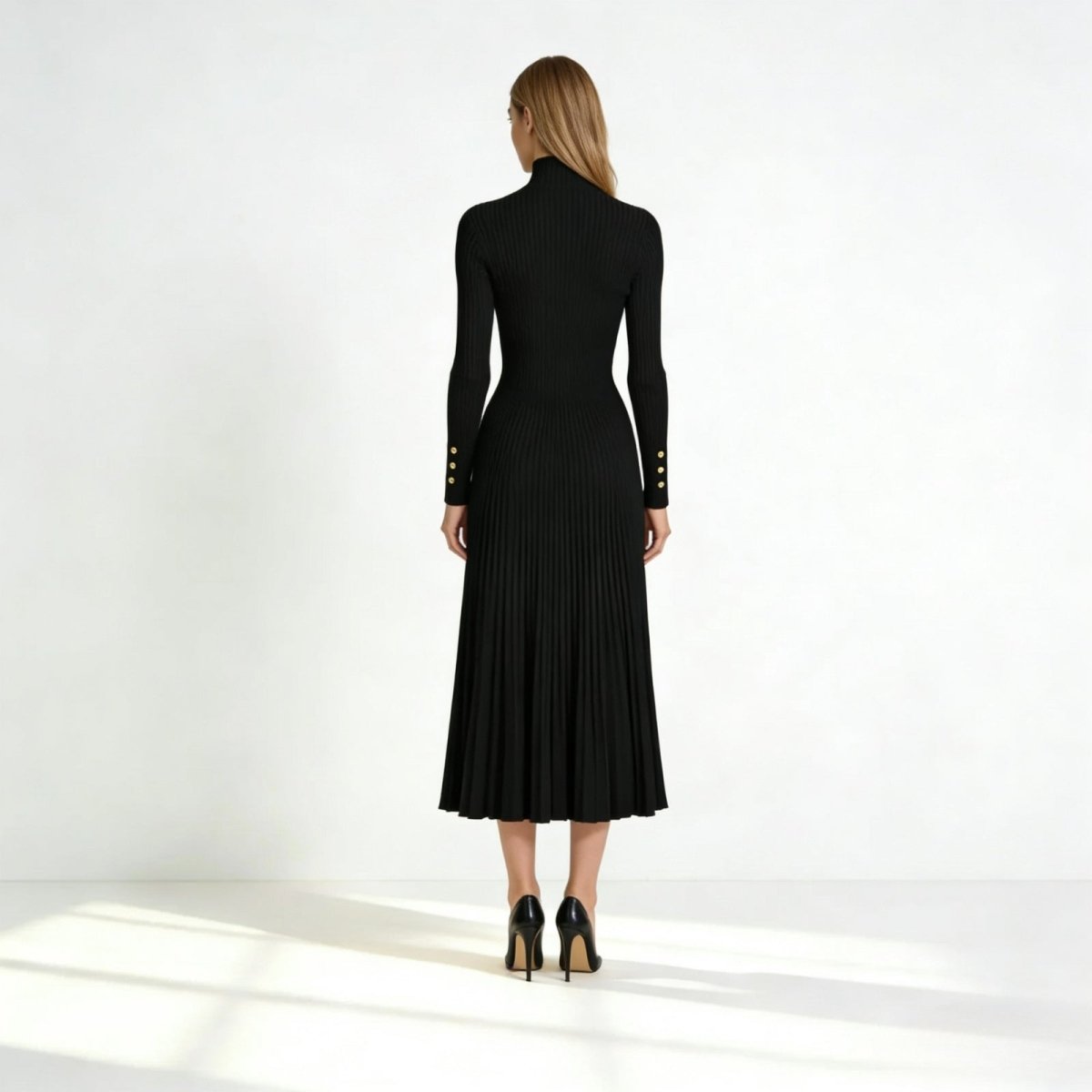 Back view of a model in the Kouvr Fashion black knit midi dress, showing the form-fitting back and flow of the pleated skirt.