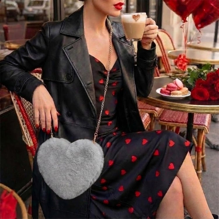 Close-up of a woman with red nails holding the soft, fluffy grey faux fur heart-shaped bag, showing its plush texture and gold chain detail.