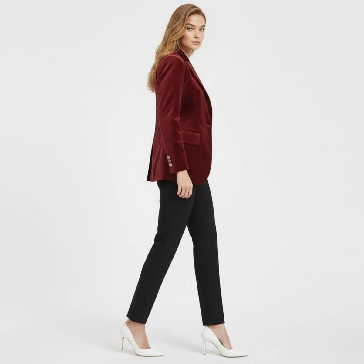 Side profile of a woman walking in a tailored wine red velvet jacket, highlighting the structured silhouette and gold cuff buttons.
