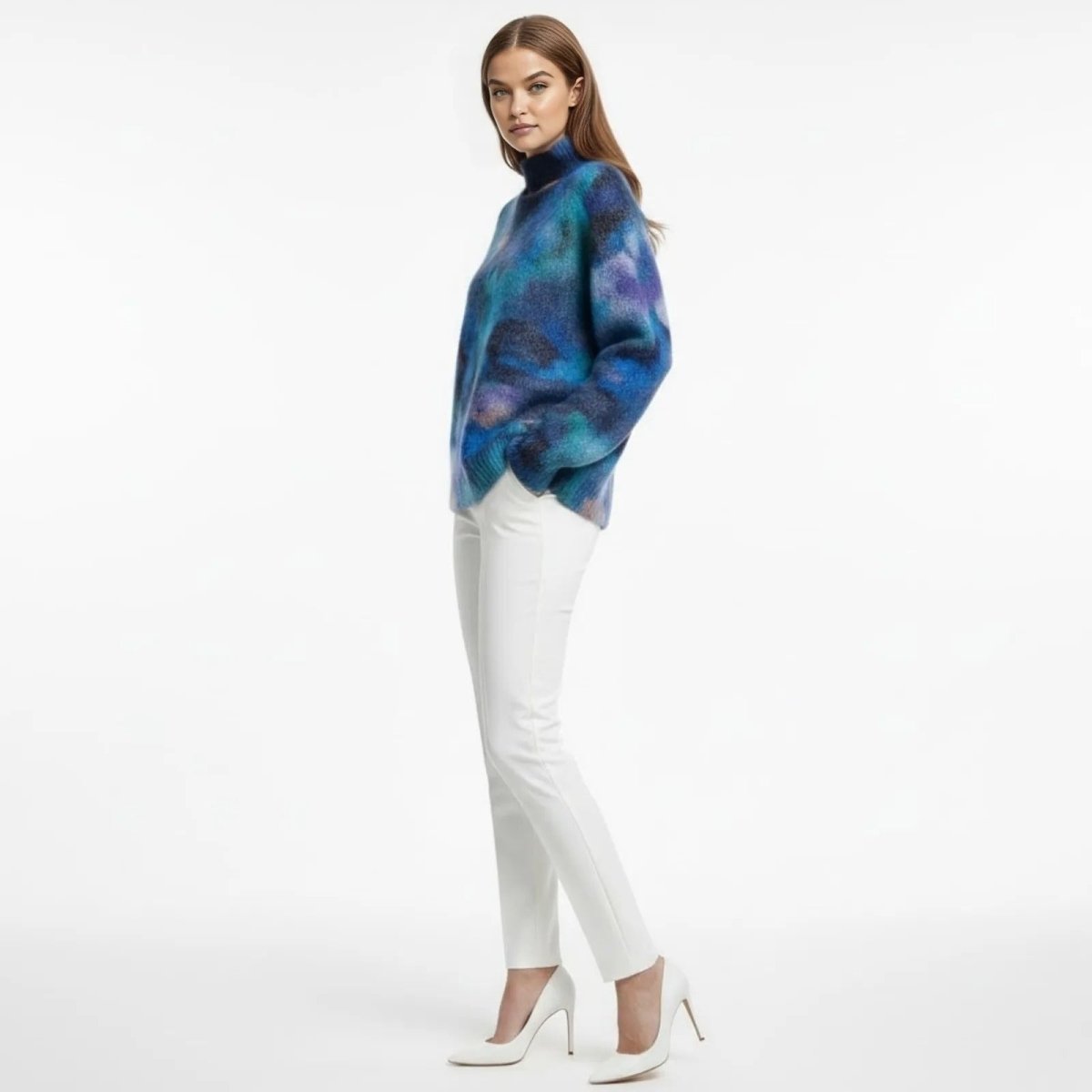 Model from the side wearing the Kouvr Fashion Regina oversized mohair turtleneck in a blue and purple abstract print, styled with white trousers and heels.