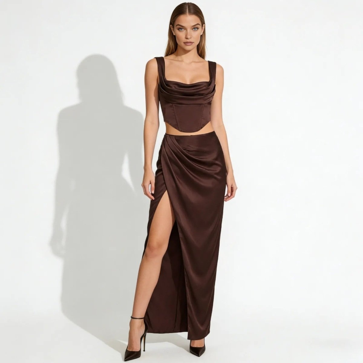 Model wearing the Rona dark brown satin set, showing the cowl neck corset top and high-slit draped maxi skirt from the front on a white background.
