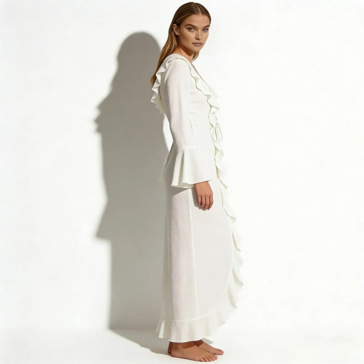 Side view of a model in the Kouvr Fashion Roseta white long sleeve ruffle beach robe, showcasing the flowing silhouette.