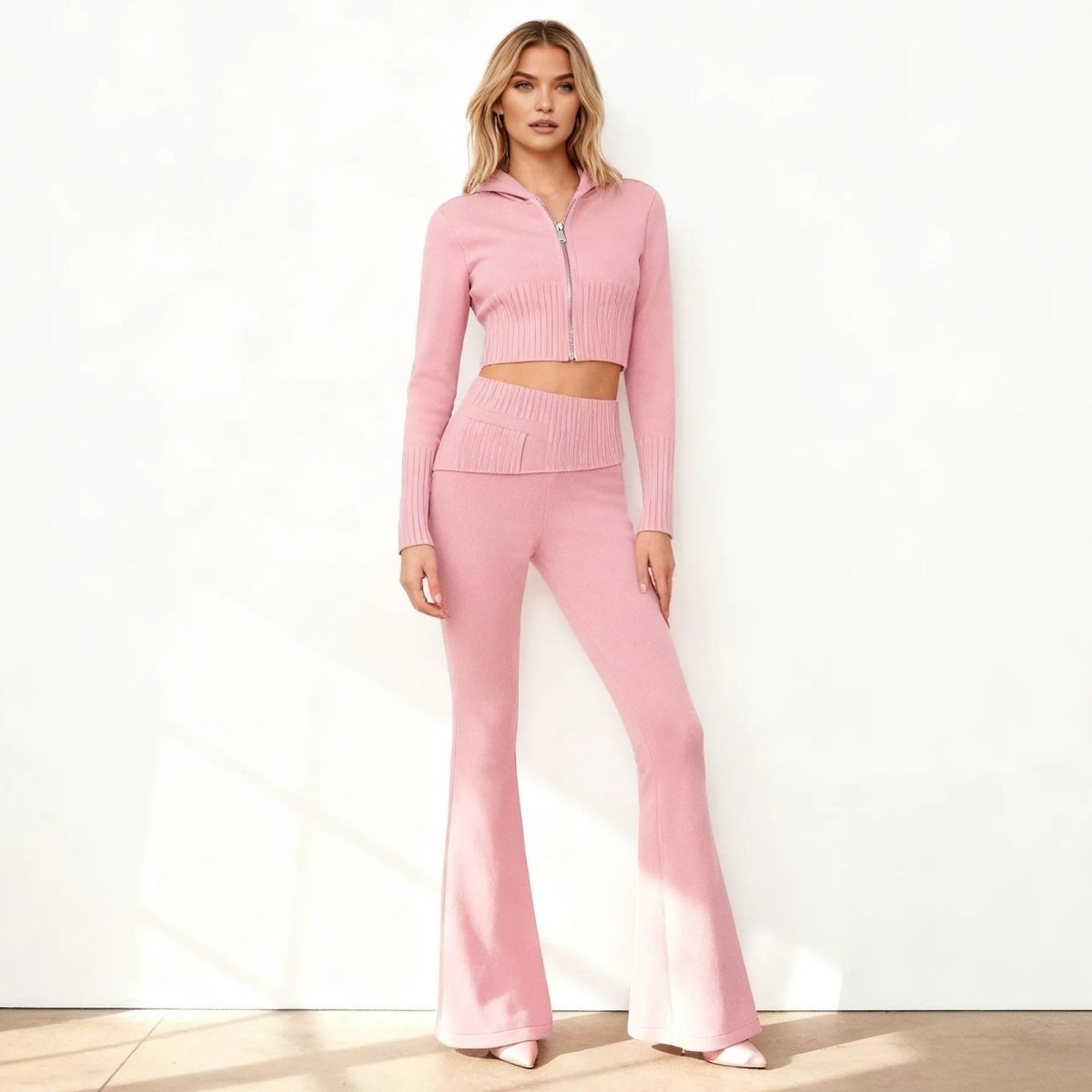 Model wearing the Kouvr Fashion rose quartz pink two-piece knit lounge set, featuring a cropped zip-up hoodie and high-waisted flared pants, shown from the front.