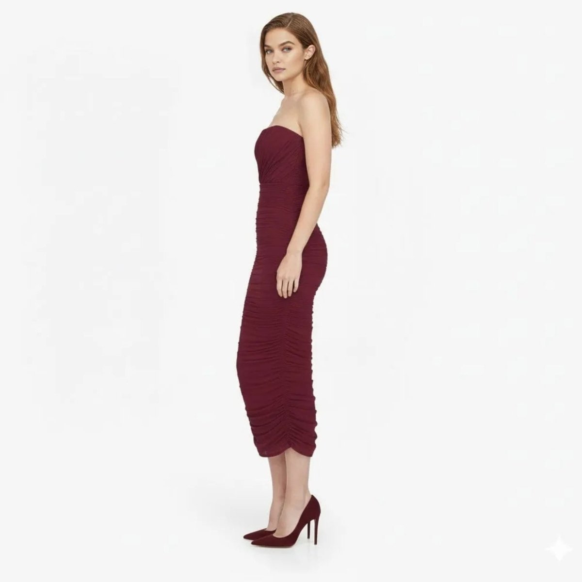 Side profile of a model in a burgundy ruched strapless cocktail dress by Kouvr Fashion showing the form-fitting silhouette.