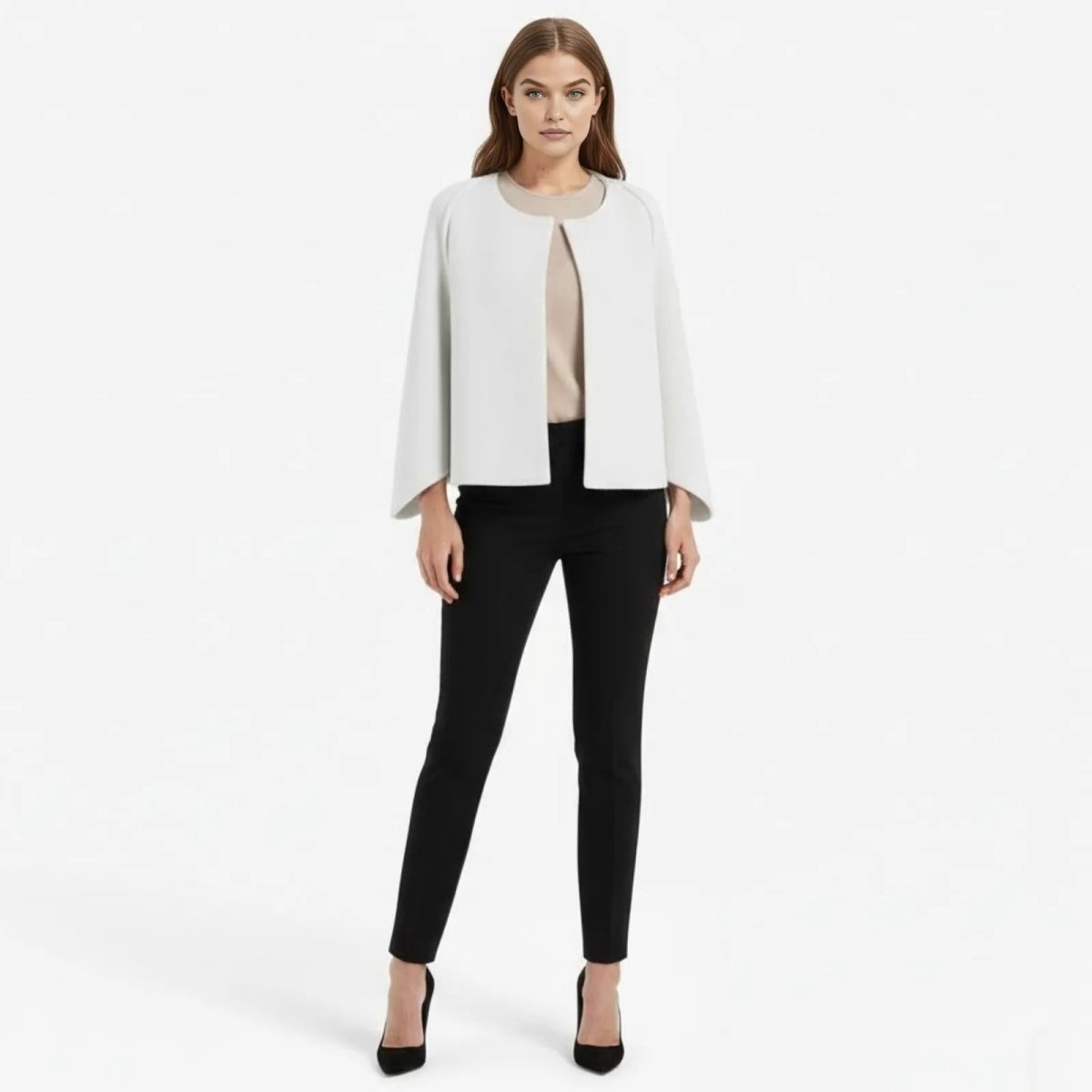 Model facing forward wearing the Kouvr Fashion white collarless cape jacket styled with black tailored pants and a neutral top.