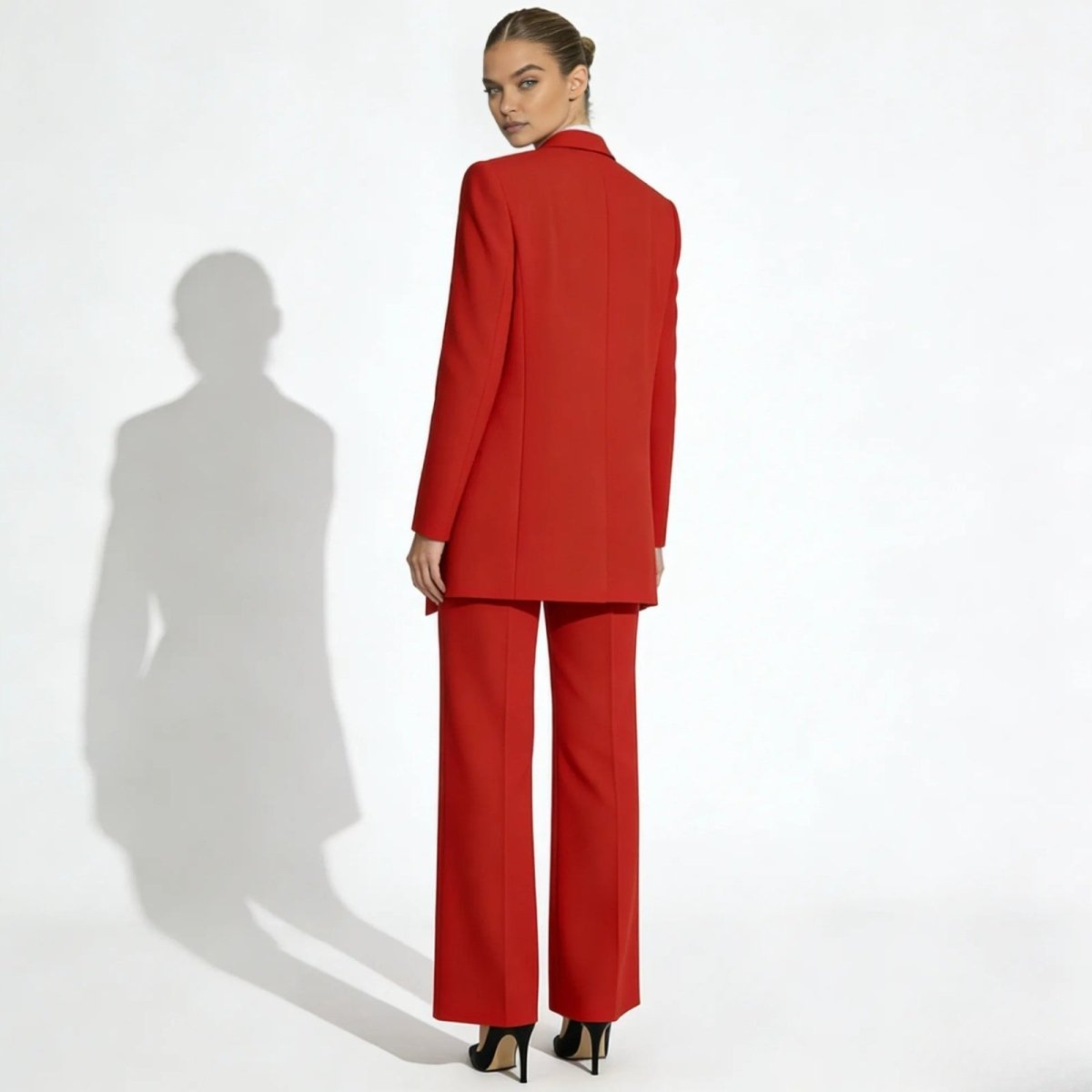 Back view of a model wearing a red suit, highlighting the structure of the blazer and the drape of the wide-leg trousers.
