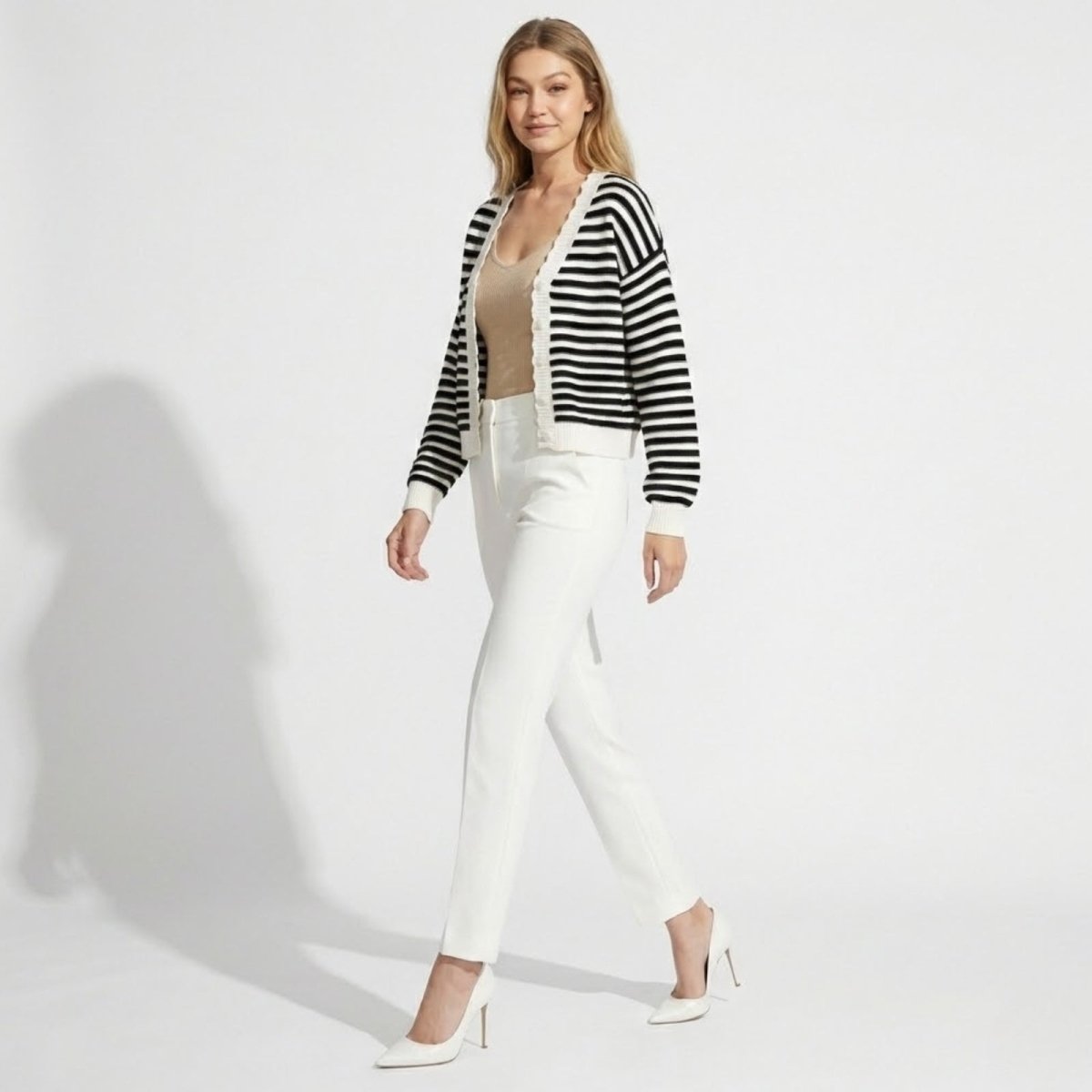 Side profile of a model walking in the Kouvr black and white striped knit cardigan, showing its relaxed fit and sleeve length.