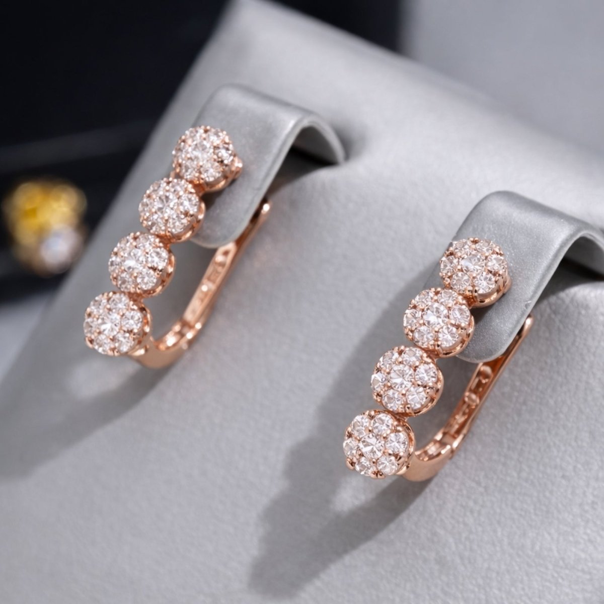 A side-angle view of the Kouvr four-stone zircon cluster earrings in 14k rose gold, presented on a sophisticated grey jewelry display.