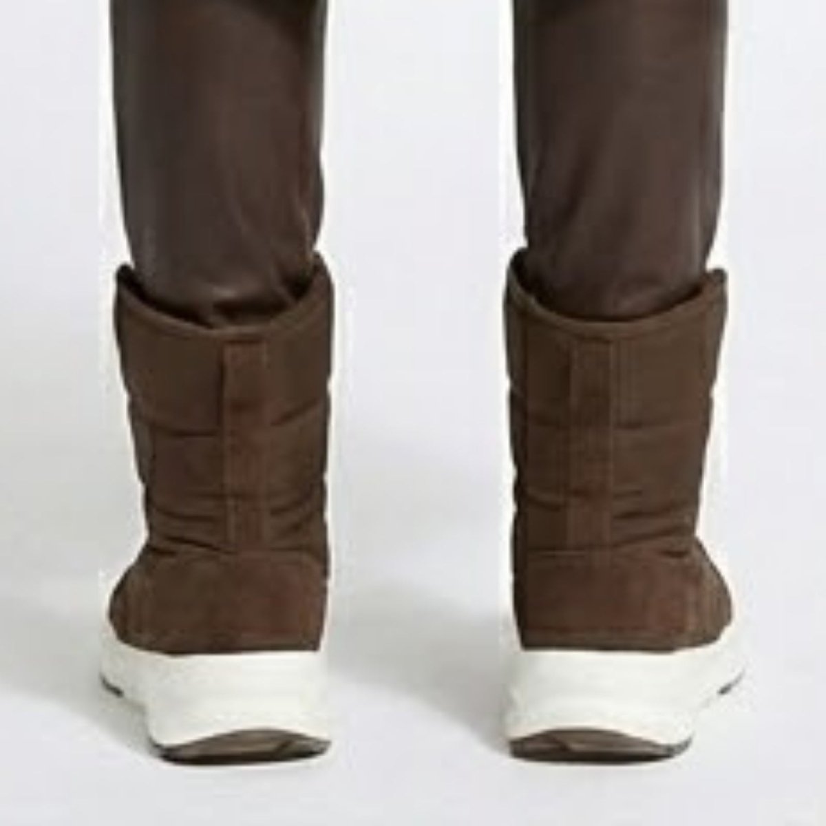 Rear view of a pair of brown quilted puffer snow boots with suede details and a thick white sole, shown on a model.