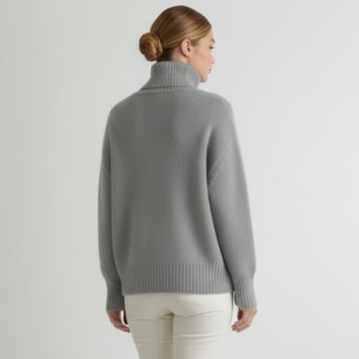 Model with her back to the camera wearing the heather grey oversized cashmere turtleneck, showing how the sweater falls.