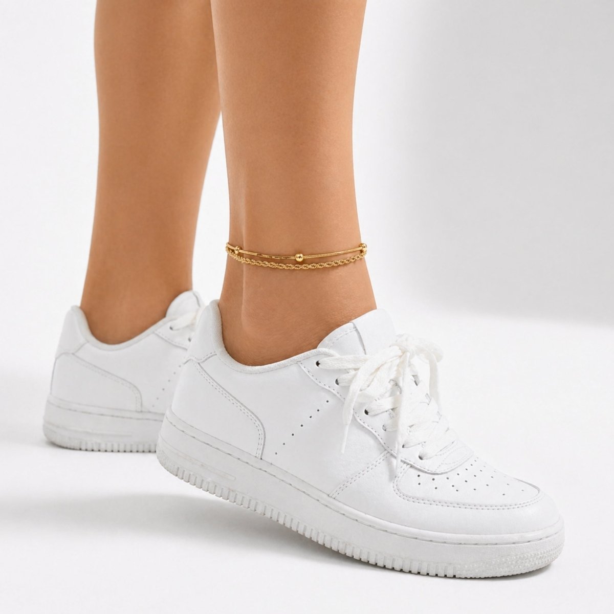 A woman walking in white sneakers, showing the styled Kouvr layered gold anklet.