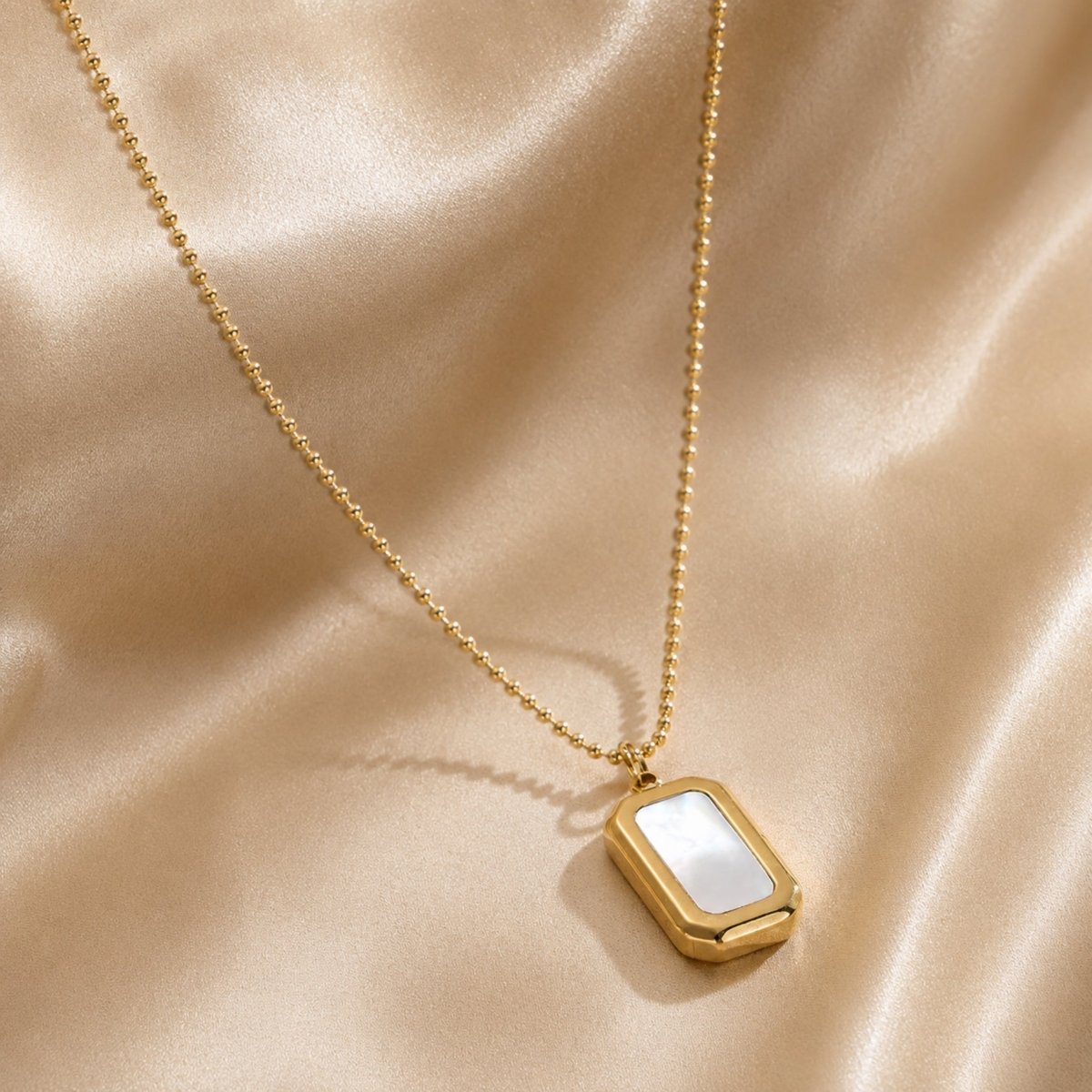 Angled detail shot of gold beaded chain necklace highlighting the iridescent white stone pendant