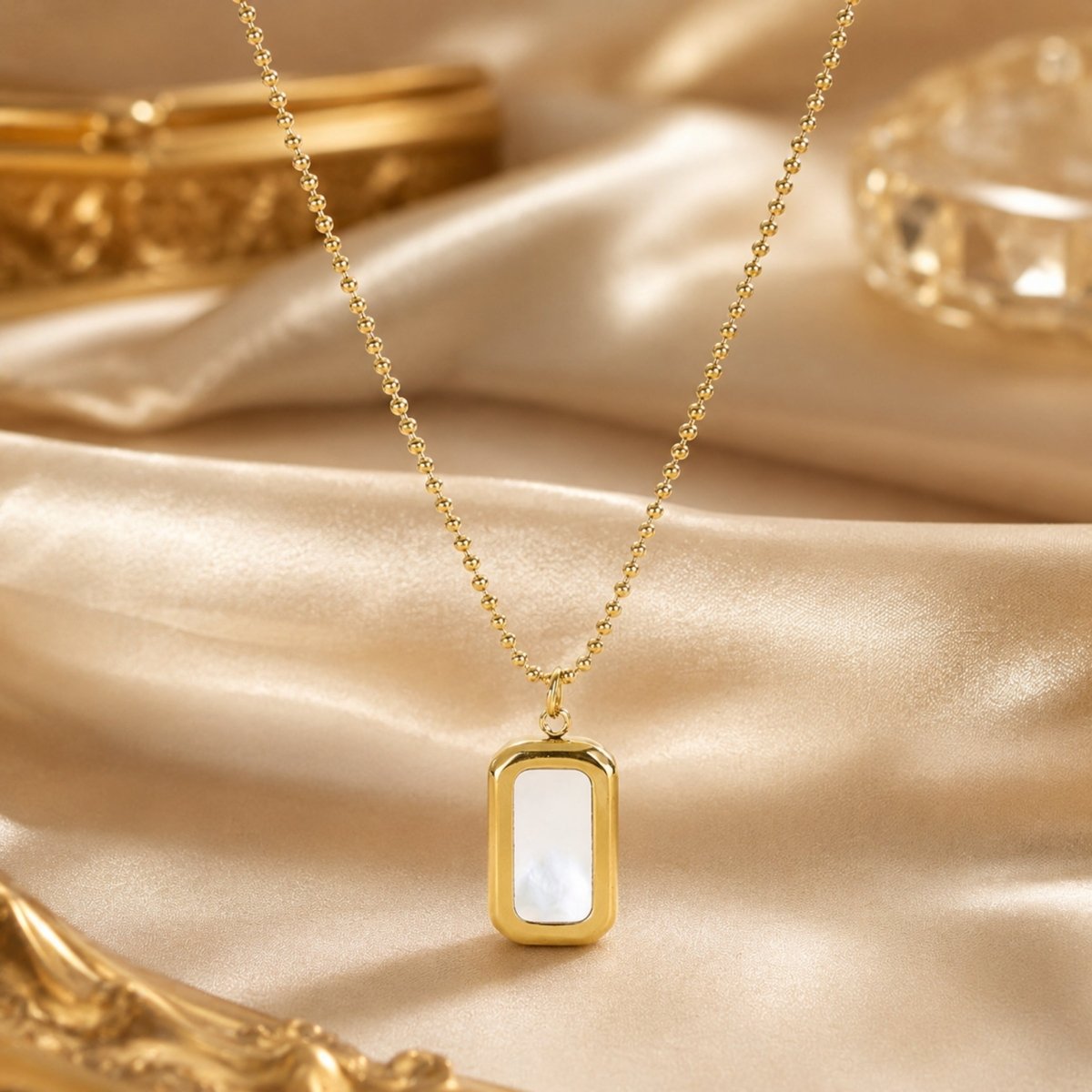 Close up of luxury gold rectangular mother of pearl necklace resting on draped champagne silk fabric