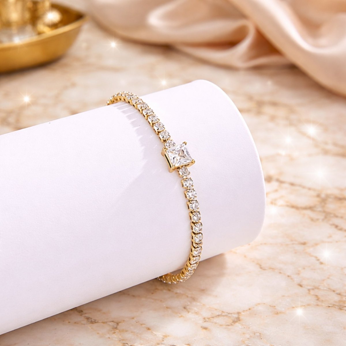 The Kouvr gold tennis bracelet with sparkling accents displayed elegantly on a white cylinder prop.
