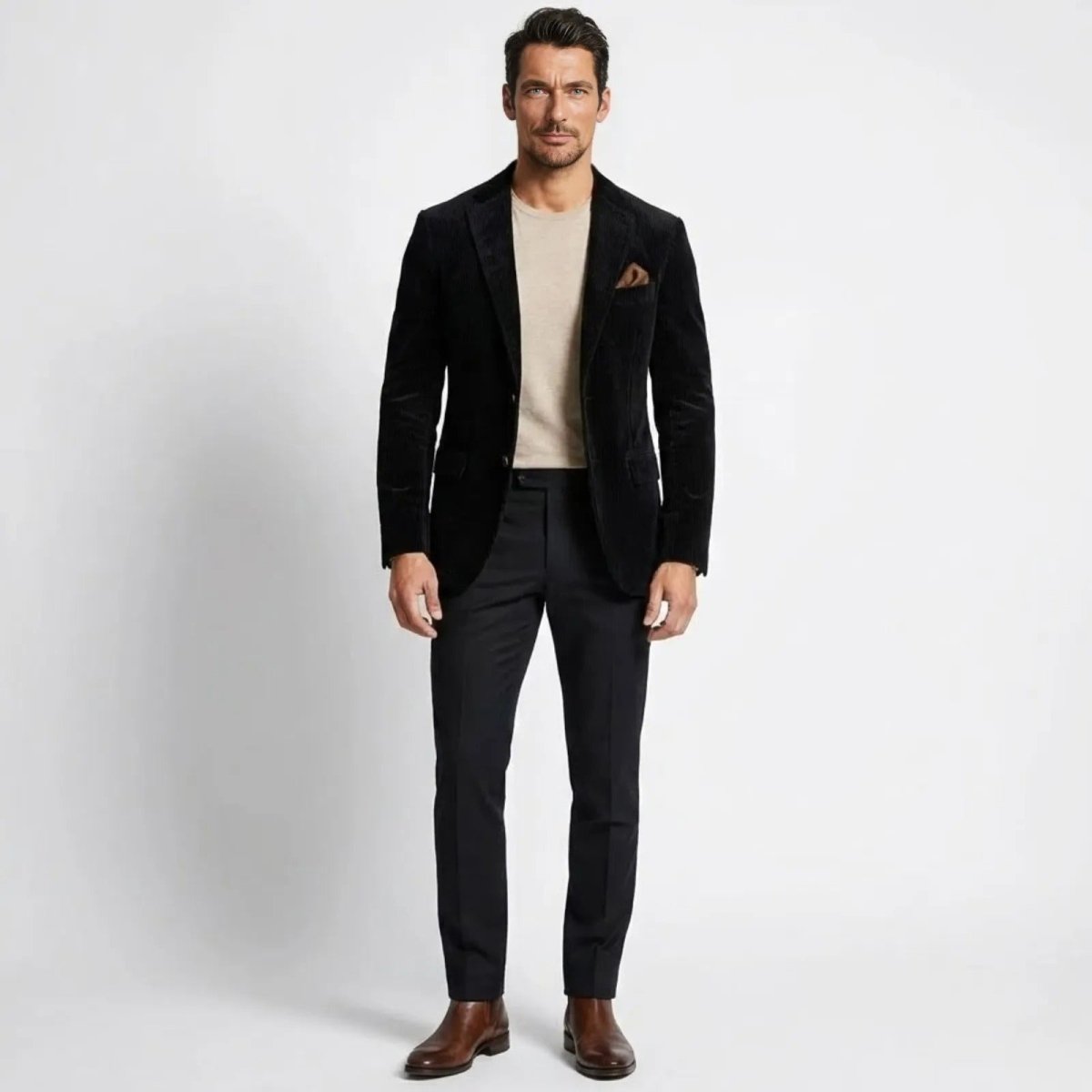 Model wearing the Kouvr Grady men's slim fit black corduroy blazer with a beige crewneck sweater and black trousers. 