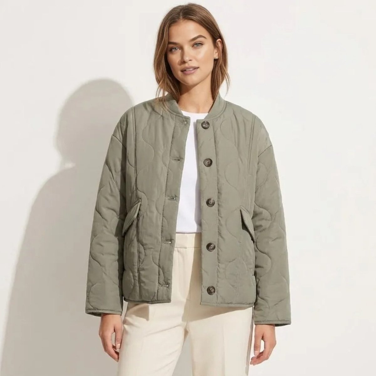 Model wearing the Kouvr Harmony sage green quilted liner jacket, buttoned over a white t-shirt and cream trousers, showing its relaxed, oversized fit.