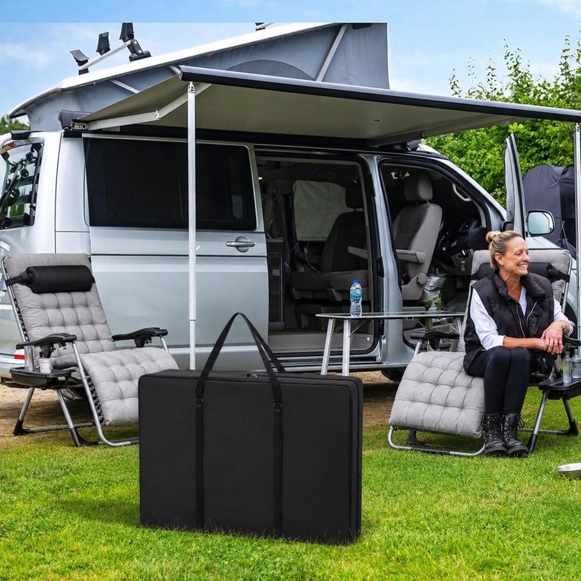 Black Kouvr heavy duty folding chair storage bag sitting on green grass next to a luxury travel RV and grey outdoor lounge chairs.