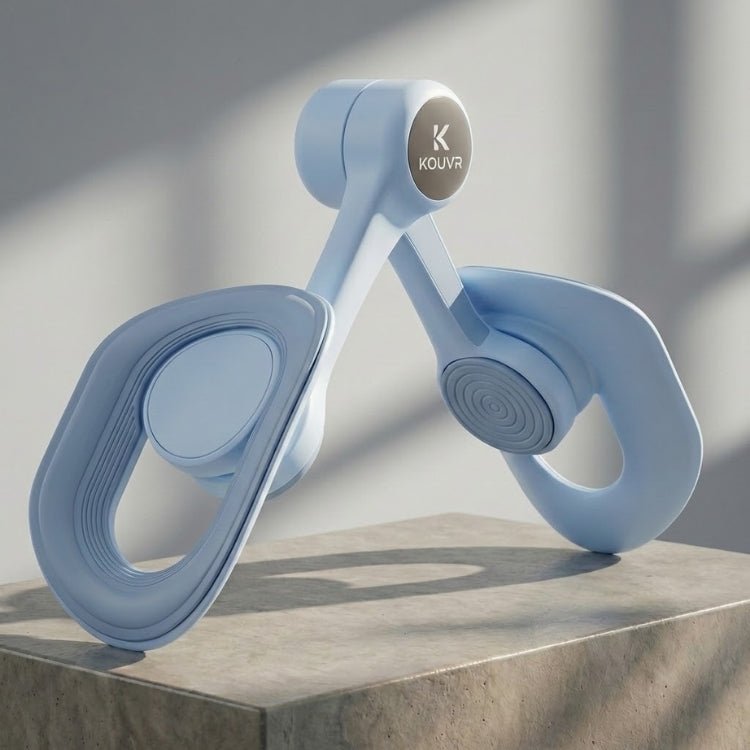 Side profile view of the blue KOUVR inner thigh toner placed on a concrete block, showing the ergonomic curved pads and the "K KOUVR" brand logo on the central hub.