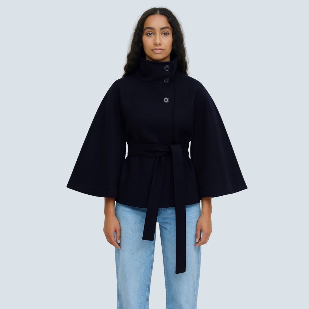 Model wearing the Kouvr Jannah Funnel Neck Wool Cape in Midnight Navy, belted at the waist and paired with light-wash denim