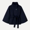 Woman wearing the Kouvr Jaye Cape in navy blue, featuring a high funnel neck, wide sleeves, and a self-tie belt