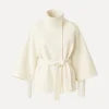 Model facing forward wears the Kouvr Jaye white wool belted cape coat with a high funnel neck and wide kimono sleeves