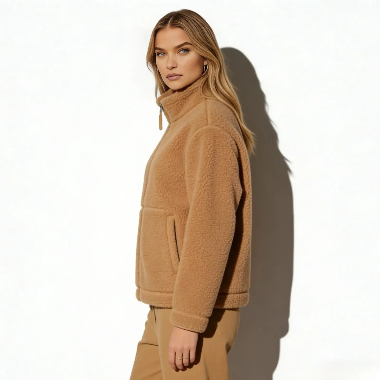 Side profile of a woman wearing the light brown tan teddy fleece zip-up jacket by Kouvr, showcasing its fit and sleeve length.