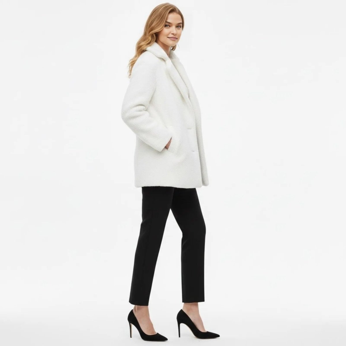 Side profile of a woman in a white sherpa peacoat from Kouvr, showing its mid-thigh length and classic silhouette.
