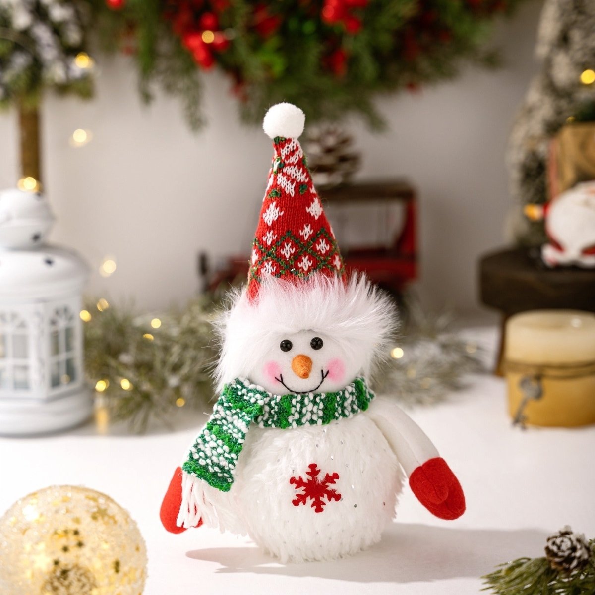 A close-up of the unlit Kouvr snowman figurine wearing a red and white patterned knit hat, a green scarf, and red mittens, highlighting its plush details.