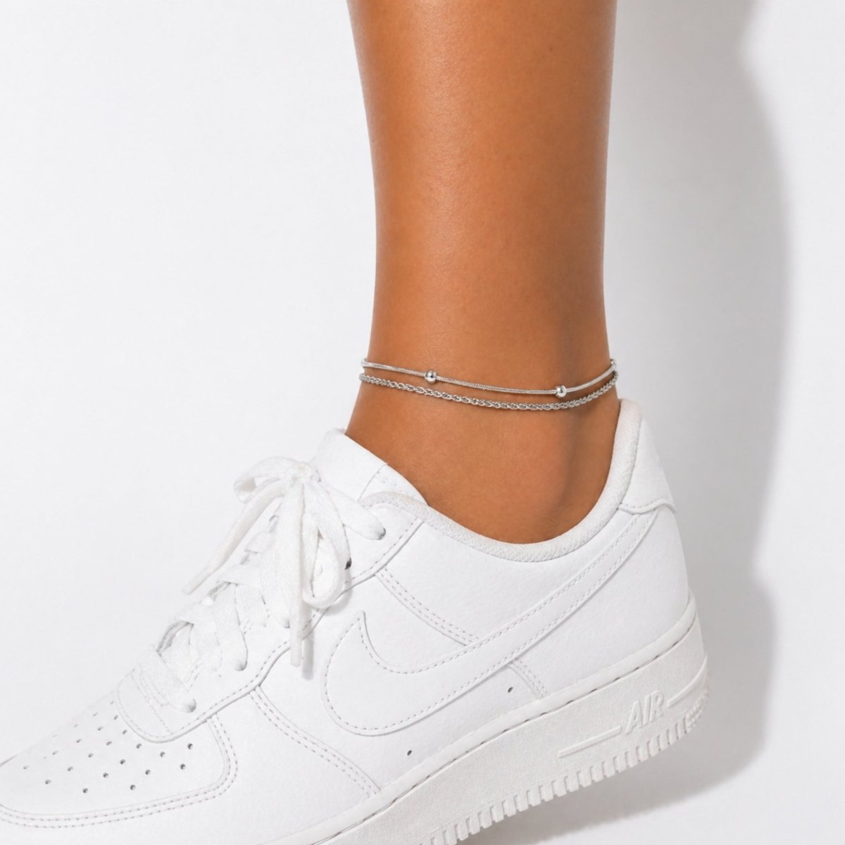 A model wearing the Kouvr double chain silver anklet, styled with fresh white sneakers.