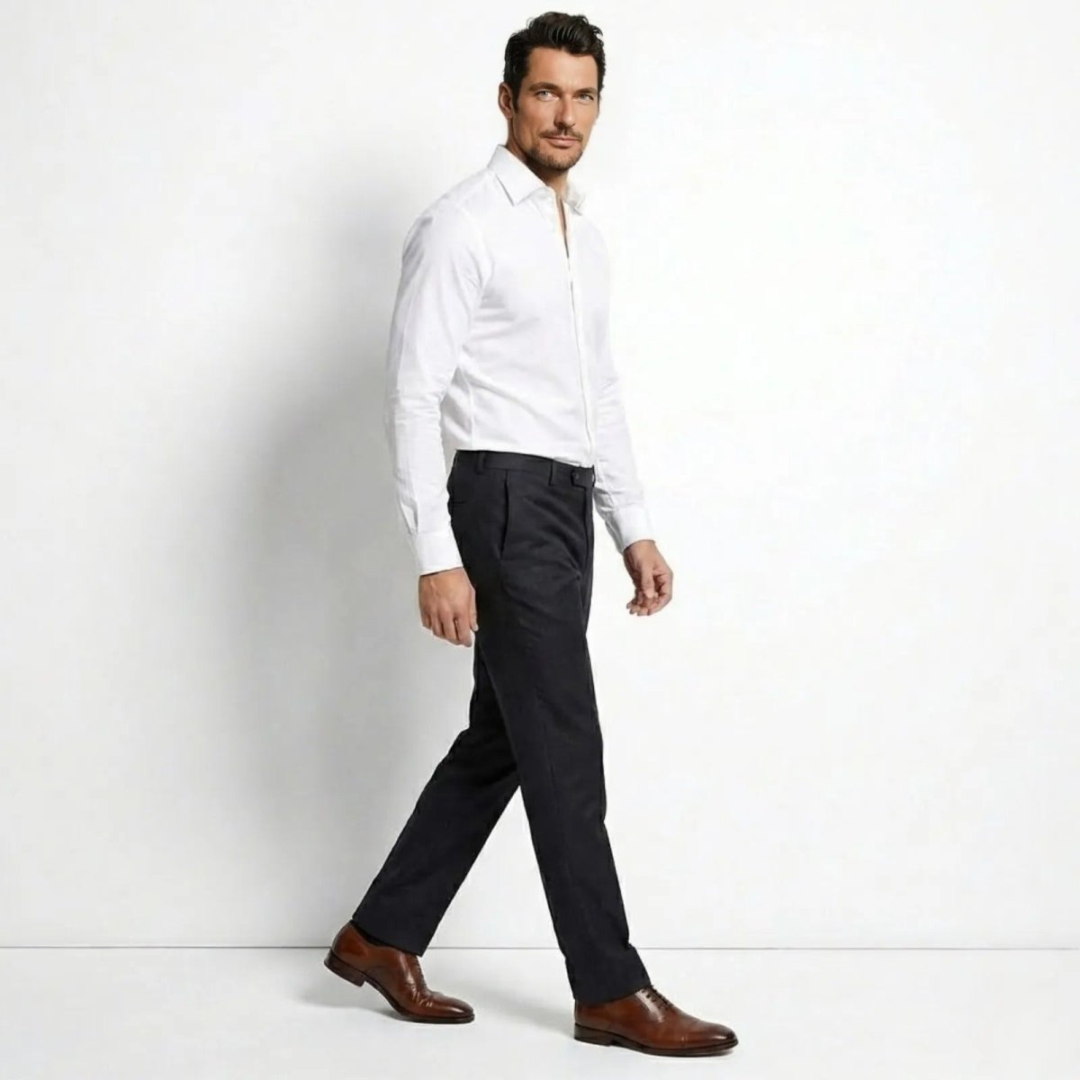 Male model in a side profile view, walking in the Kouvr Leland White Dress Shirt, showcasing its tailored fit and drape.

