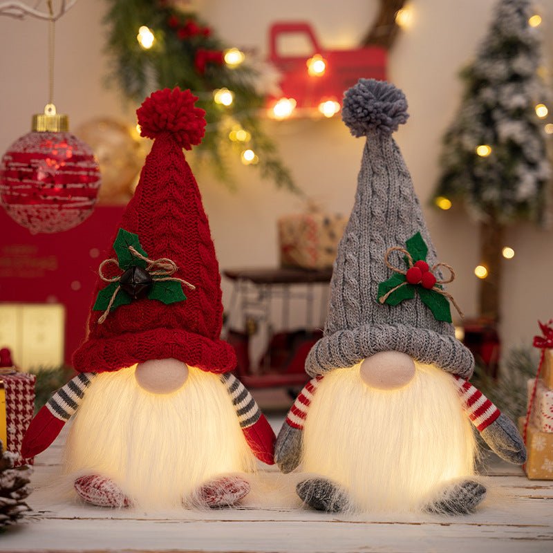 A pair of light-up Christmas gnomes, one with a red knit hat and one with a grey knit hat, sitting on a wooden surface with their white beards glowing warmly amidst festive holiday decor.