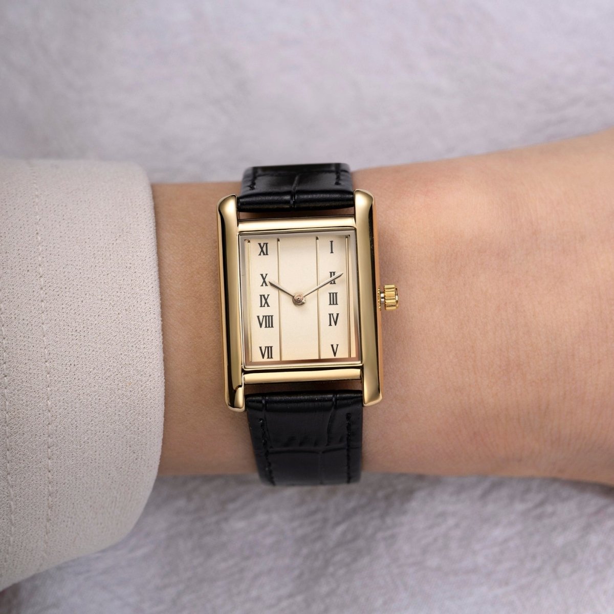 Gold kouvr watch with black strap on a wrist against a neutral background